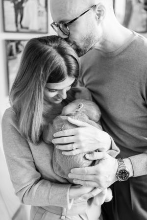 A tender family moment with parents embracing their newborn in black and white.