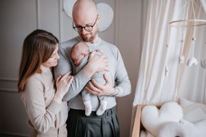 Parents in neutral tones holding their newborn baby near a white balloon display.