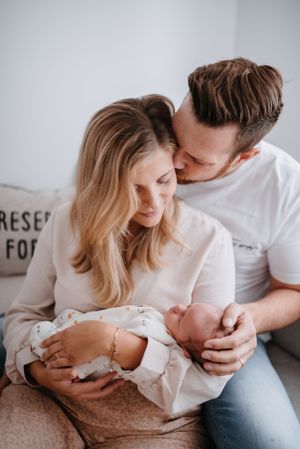 Intimate family moment with parents cuddling their newborn baby on a couch.