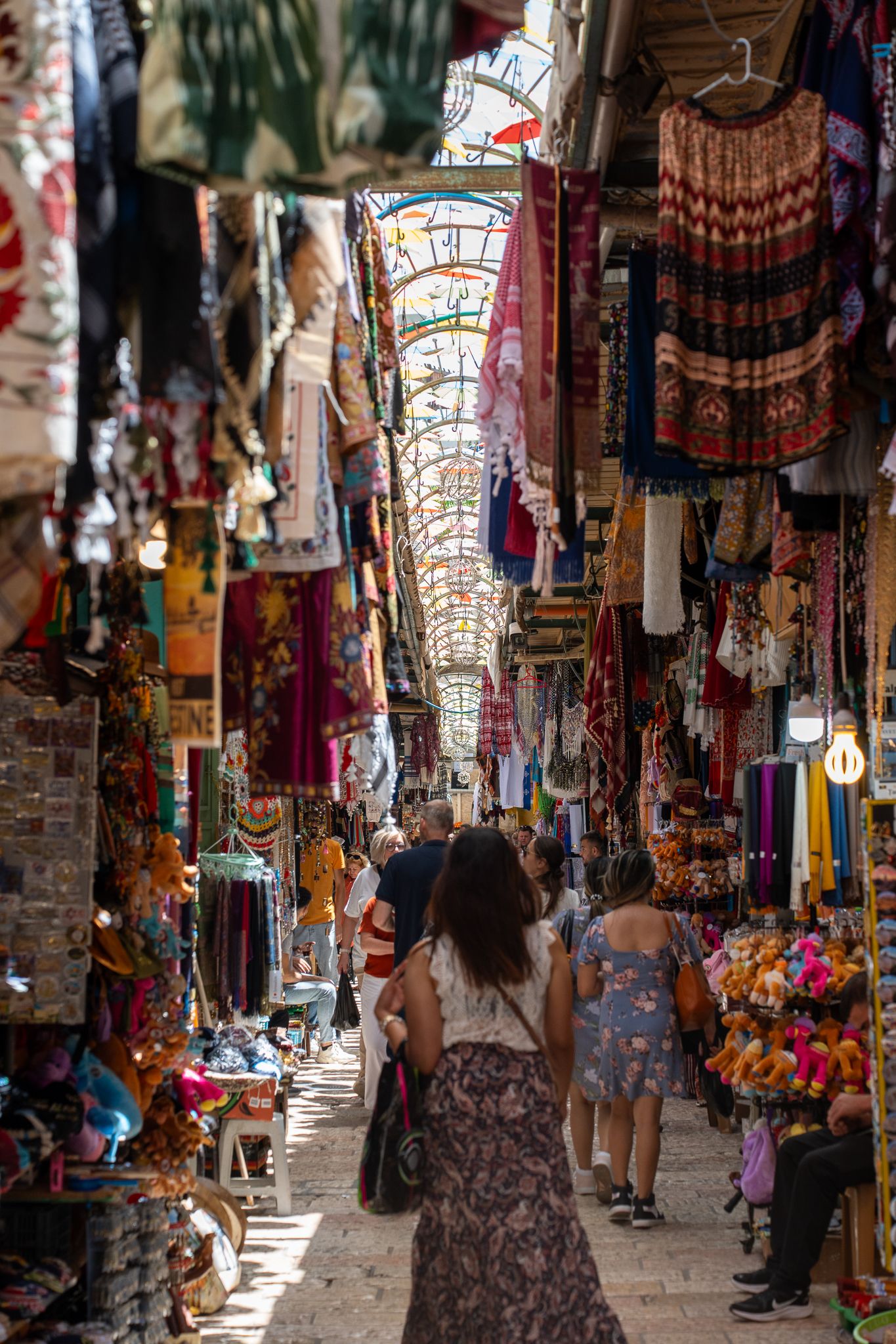 Narrow marketplace corridor lined with colorful textiles and souvenirs in a Middle Eastern bazaar.