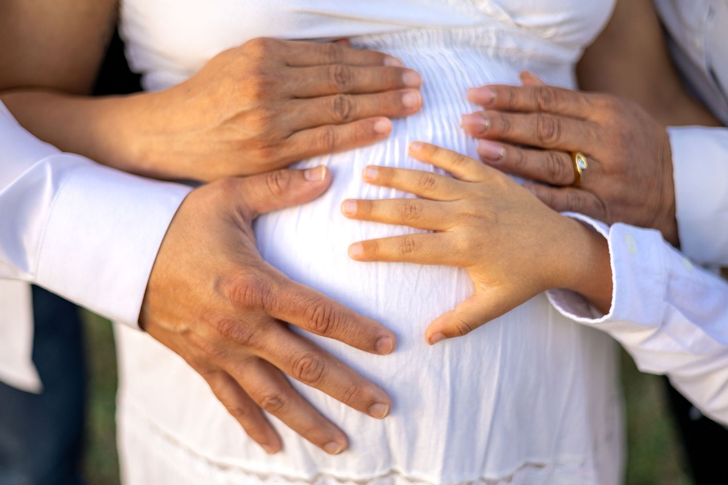 Close-up of hands forming a heart shape on a pregnant belly in white dress.