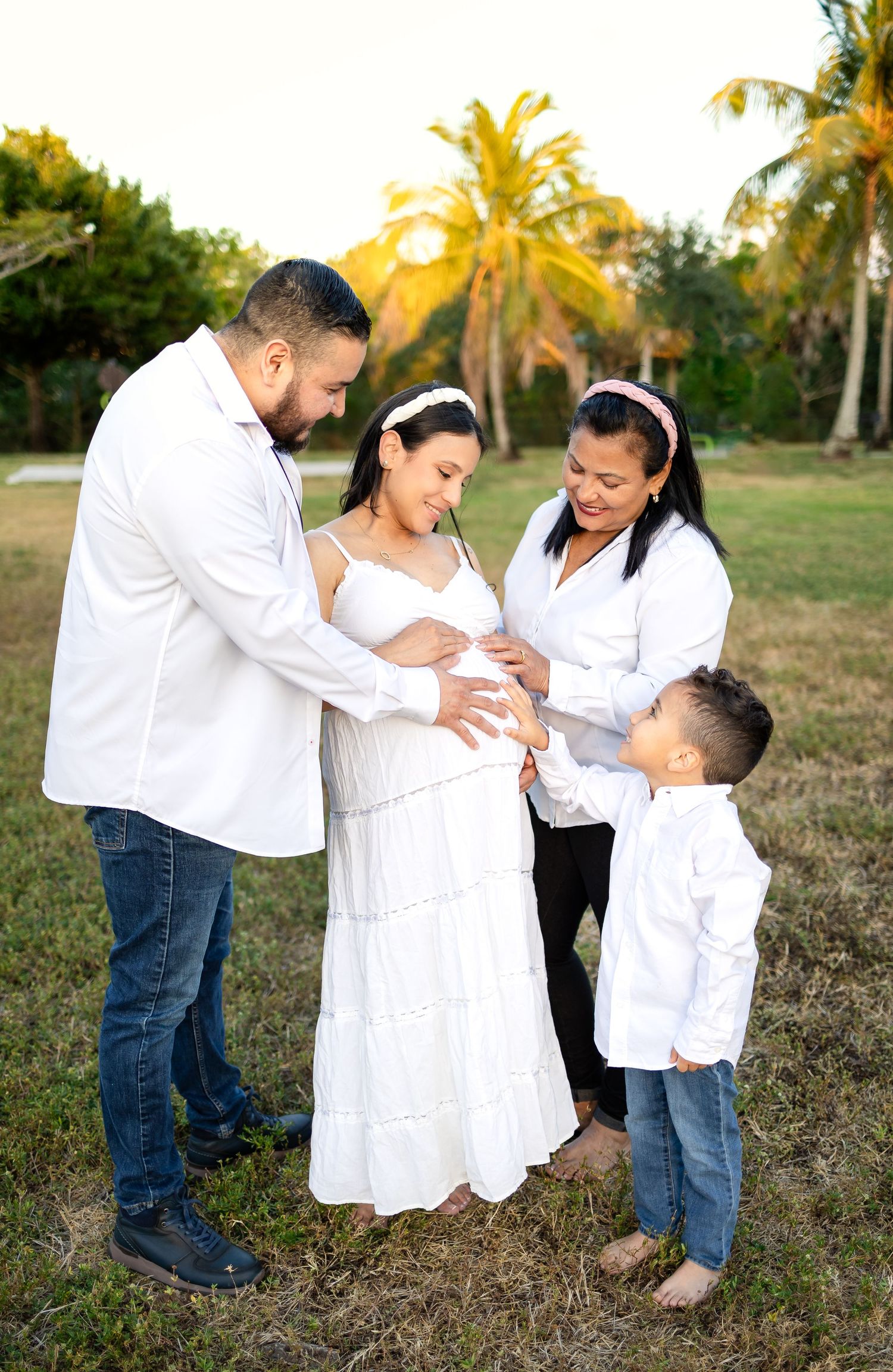 A family gathering outdoors for a maternity photo shoot with palm trees in the background.
