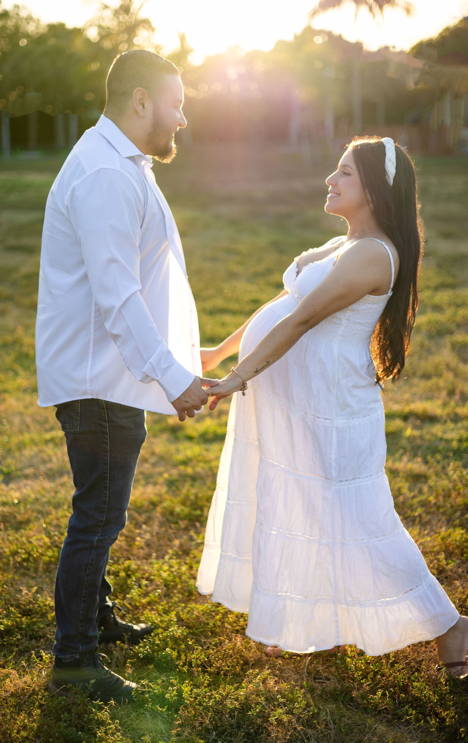 A couple holds hands during their maternity photoshoot at sunset with palm trees in background.
