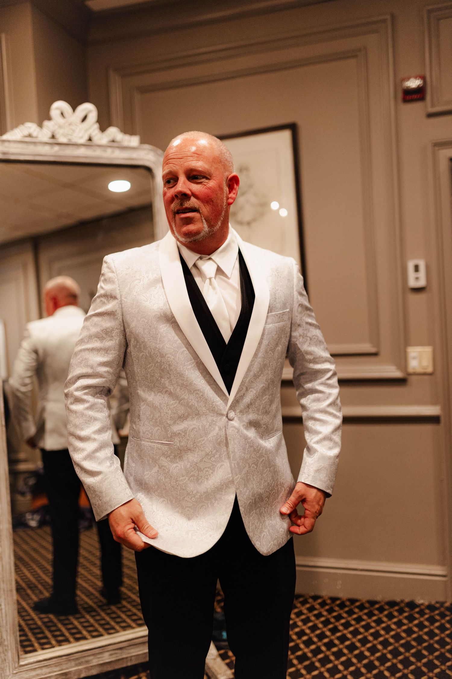 Wedding party members in white tuxedo jackets and black pants pose in an elegant indoor venue.