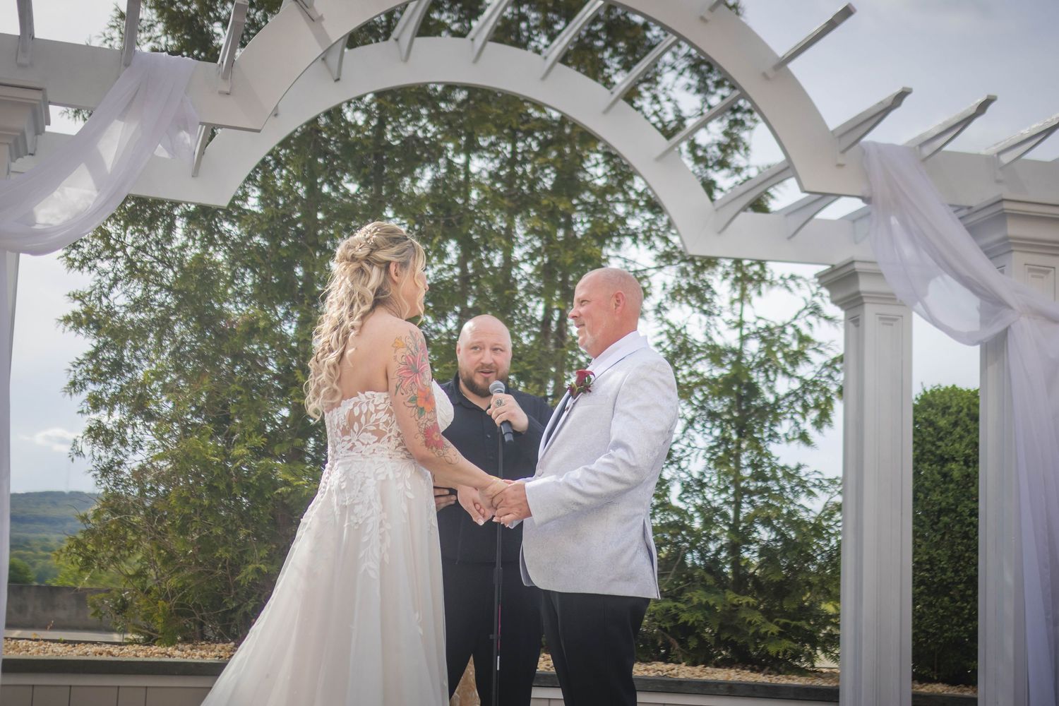 Wedding ceremony taking place under a white pergola with scenic mountain backdrop.
