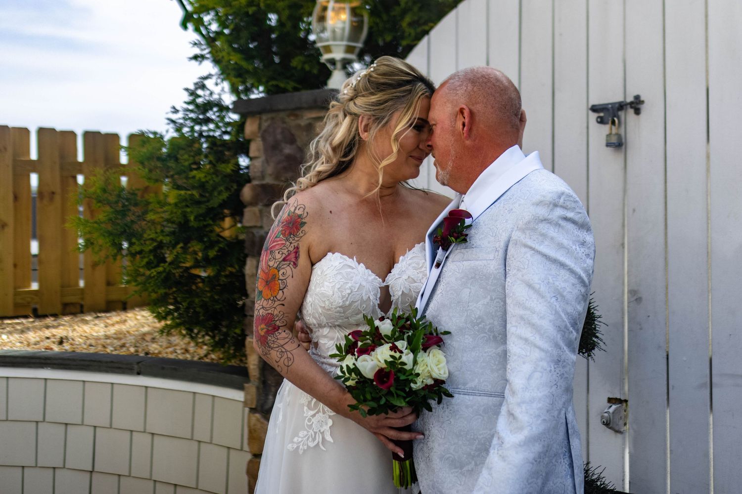 Wedding couple shares intimate moments against white fence backdrop during outdoor photo session.