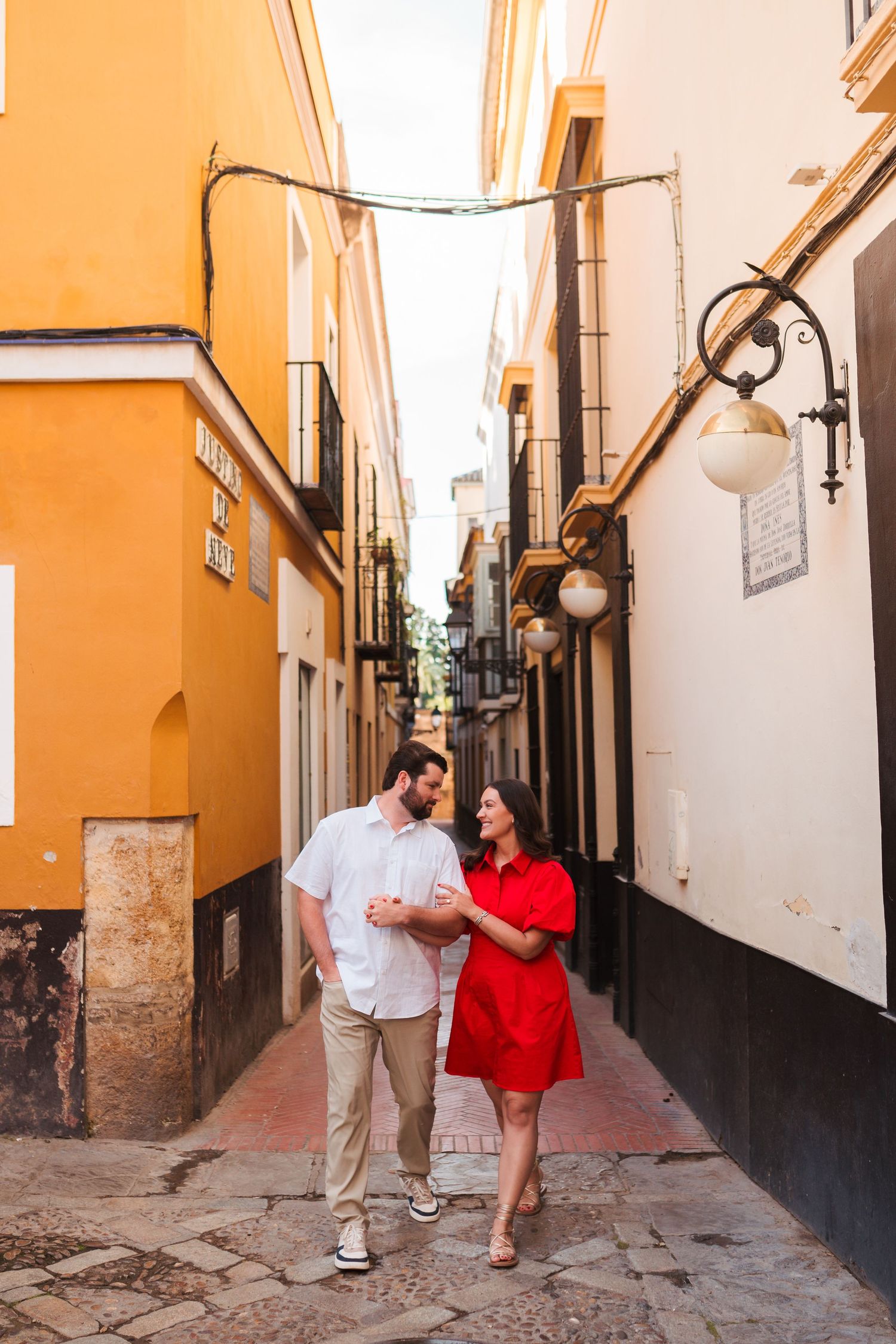 Couple embracing in a garden setting with iron fence and brick wall backdrop.