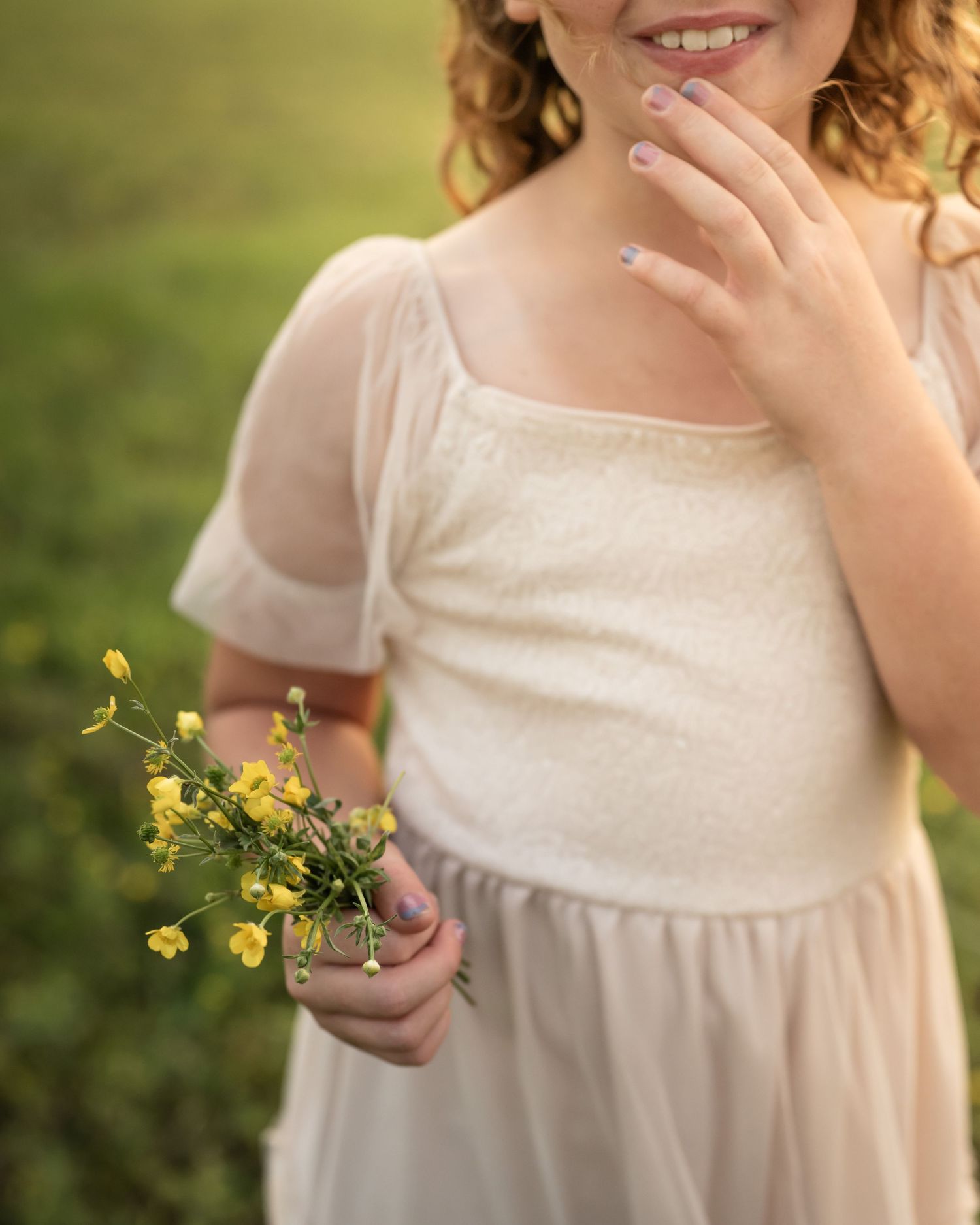 Young person in white dress holding delicate yellow wildflowers in a sunlit field.