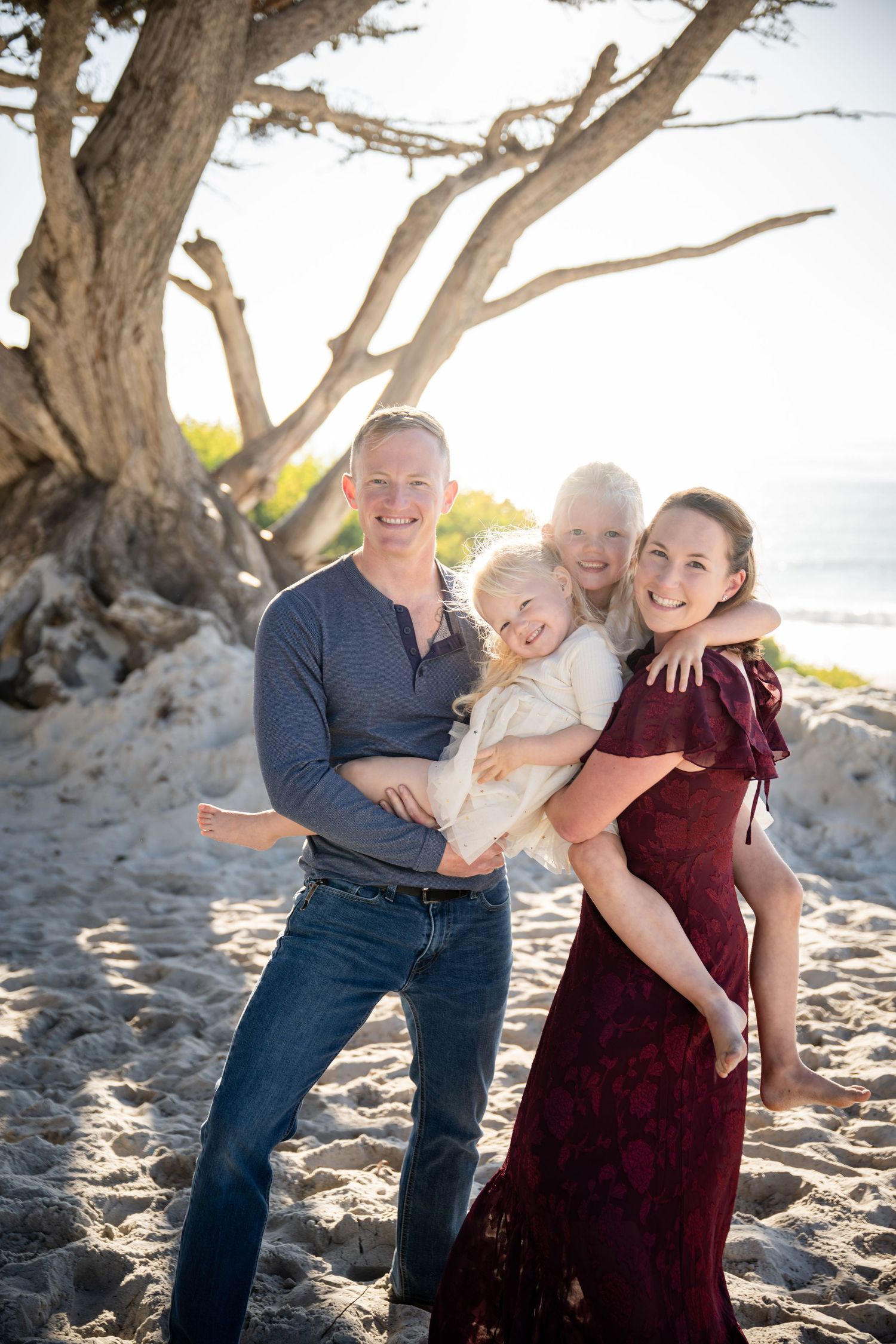 Family shares joyful moments under beach trees during sunset photoshoot.