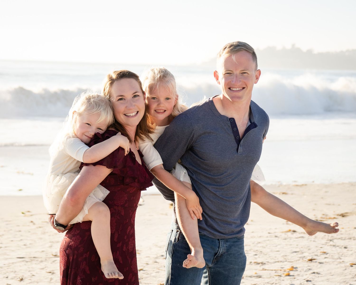 Playful family moment captured on sunny beach with ocean backdrop.