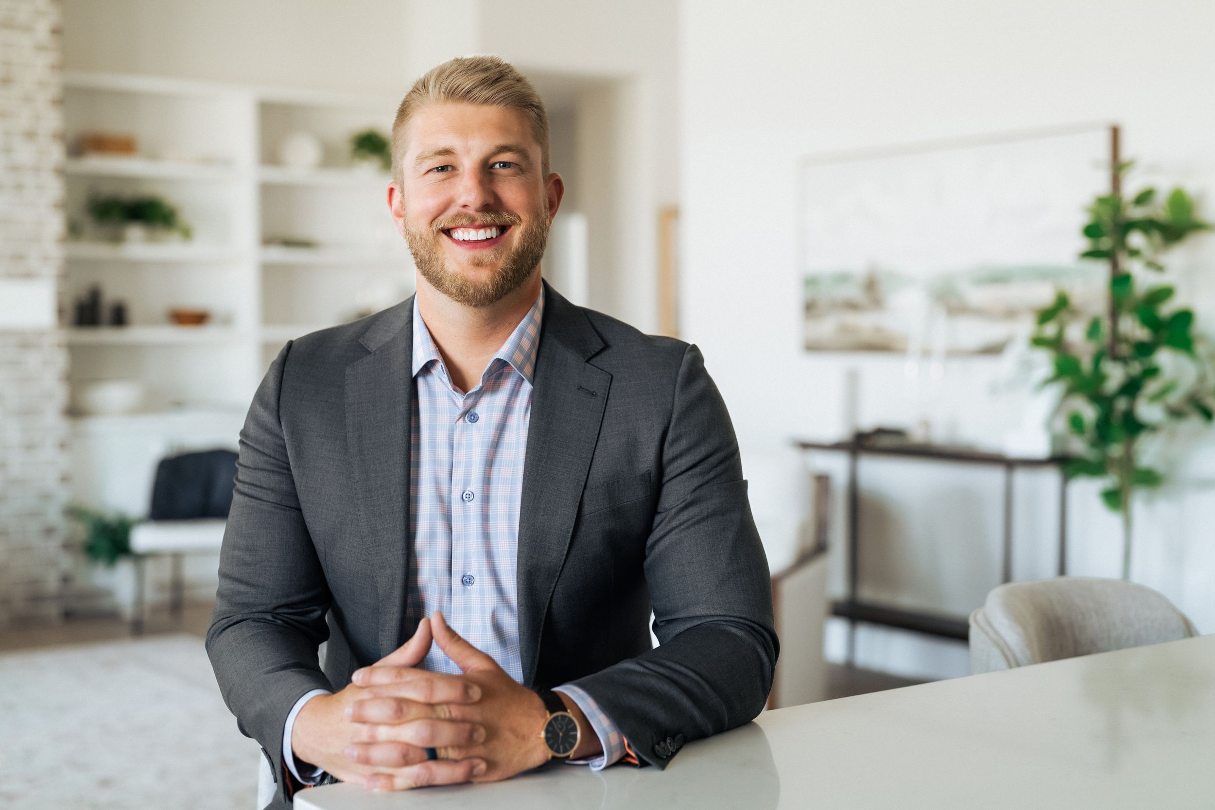 Smiling businessman in gray suit sitting at white table in modern bright office interior.