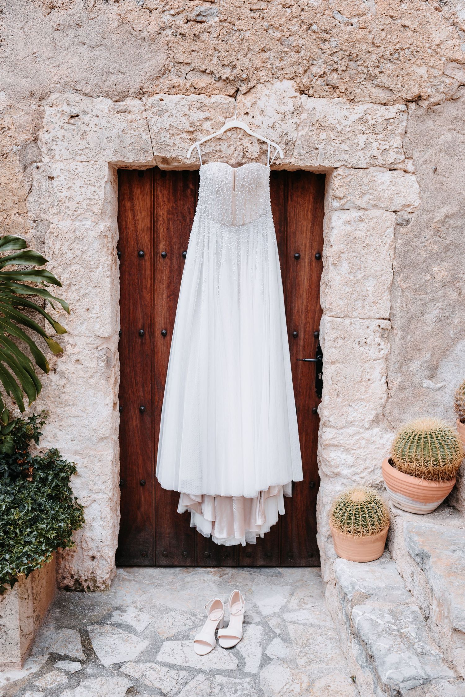 Weißes Hochzeitskleid hängt an einer rustikalen Tür, eines mallorquinischen Hauses, in einem mediterranen Innenhof.