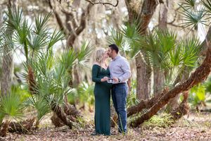 A couple stands together in a romantic pose among palm trees and live oaks in a lush tropical setting.