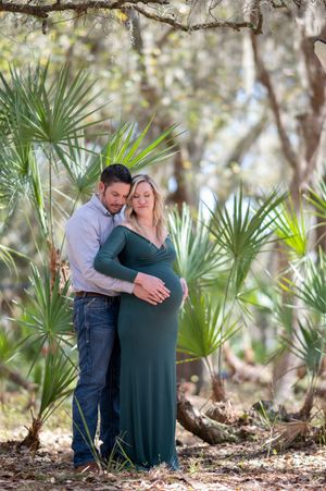 Couple embraces in romantic outdoor photo session surrounded by lush palm trees and natural lighting.