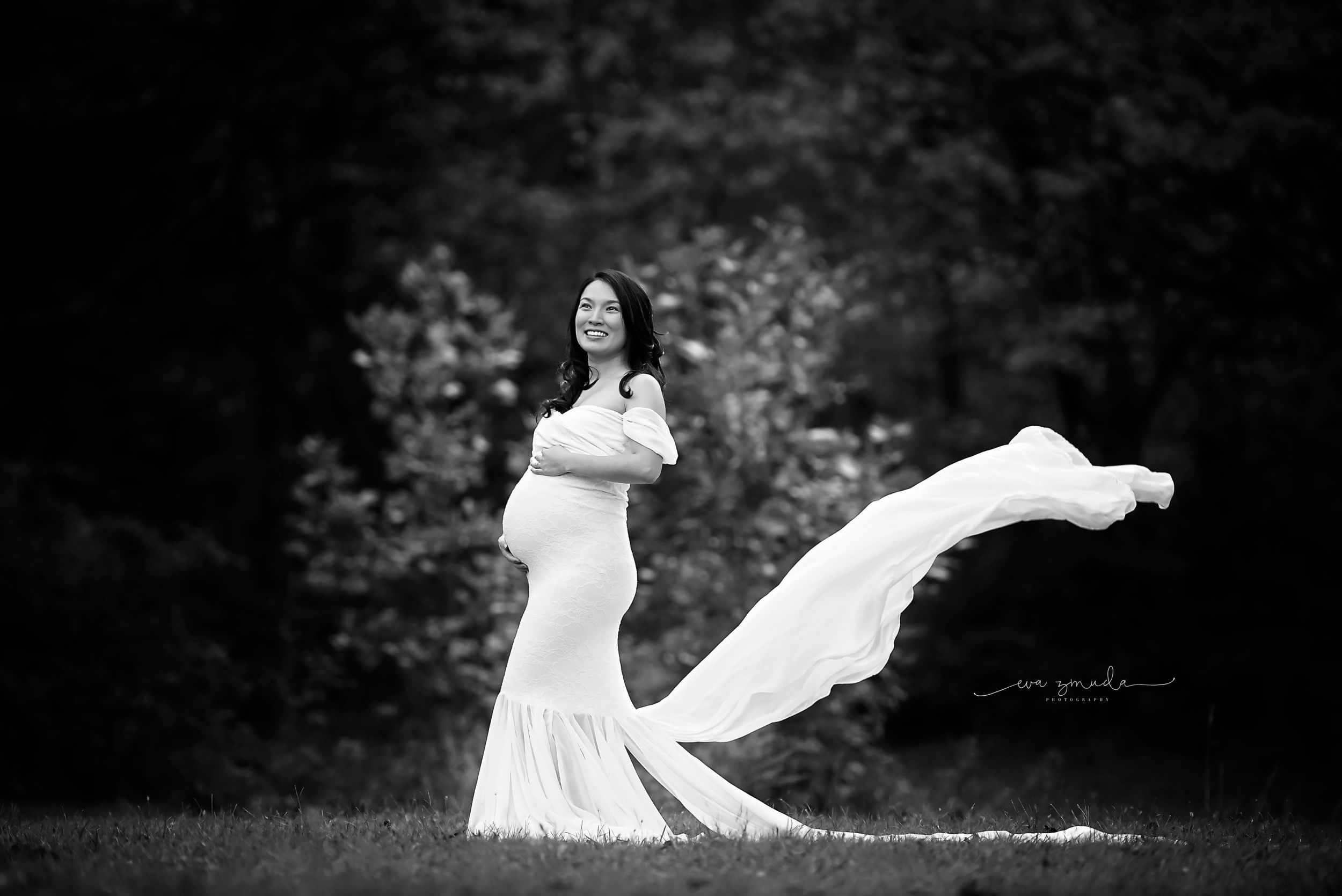 Dramatic black and white maternity photo with flowing dress in outdoor setting.