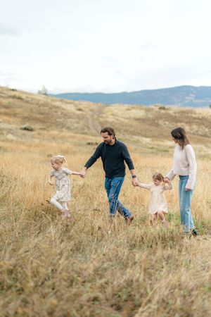 Family walking together through tall golden grass on a hillside with mountains in the background on an autumn day.