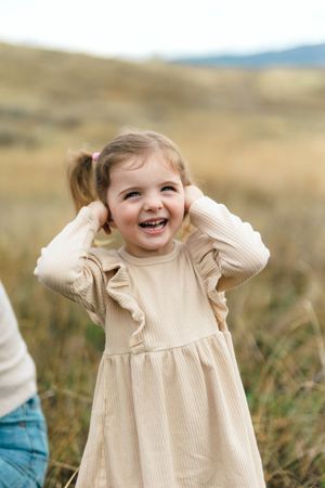 Child wearing cream-colored ribbed dress plays joyfully in grassy field on autumn day.
