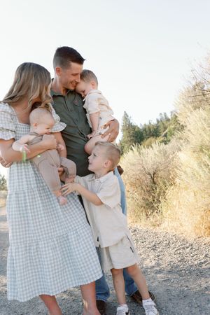 A family shares a tender moment together outdoors on a dirt path surrounded by dry grass and trees.
