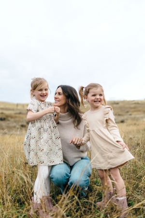 Family shares joyful moment together while standing in tall grass field during golden hour.