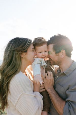 A family shares a tender moment together in warm sunlight, with everyone leaning in close to embrace their young child.