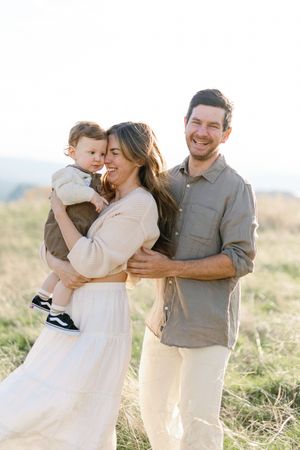 A family in white and neutral clothing shares joyful moments together in a grassy field at sunset.