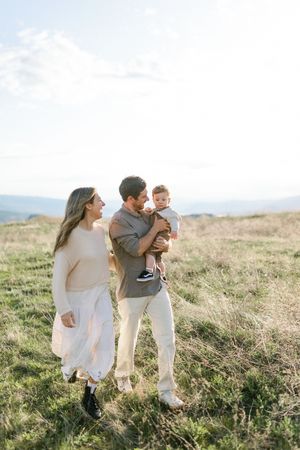 A family in white clothing walks together through a golden field at sunset, sharing joyful moments.