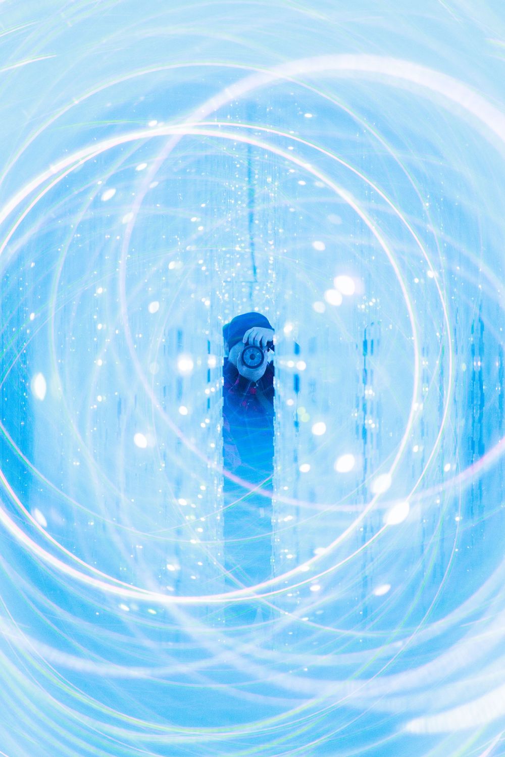 Ethereal swirling blue and white circular patterns create a mesmerizing tunnel effect against a light background.