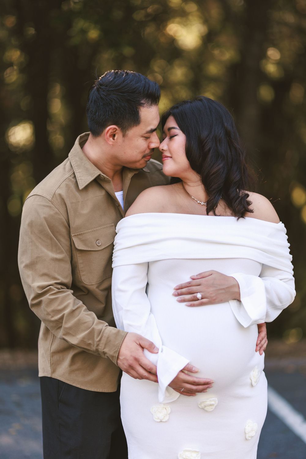 A romantic couple embraces tenderly in a series of intimate outdoor maternity photos wearing white and tan outfits.