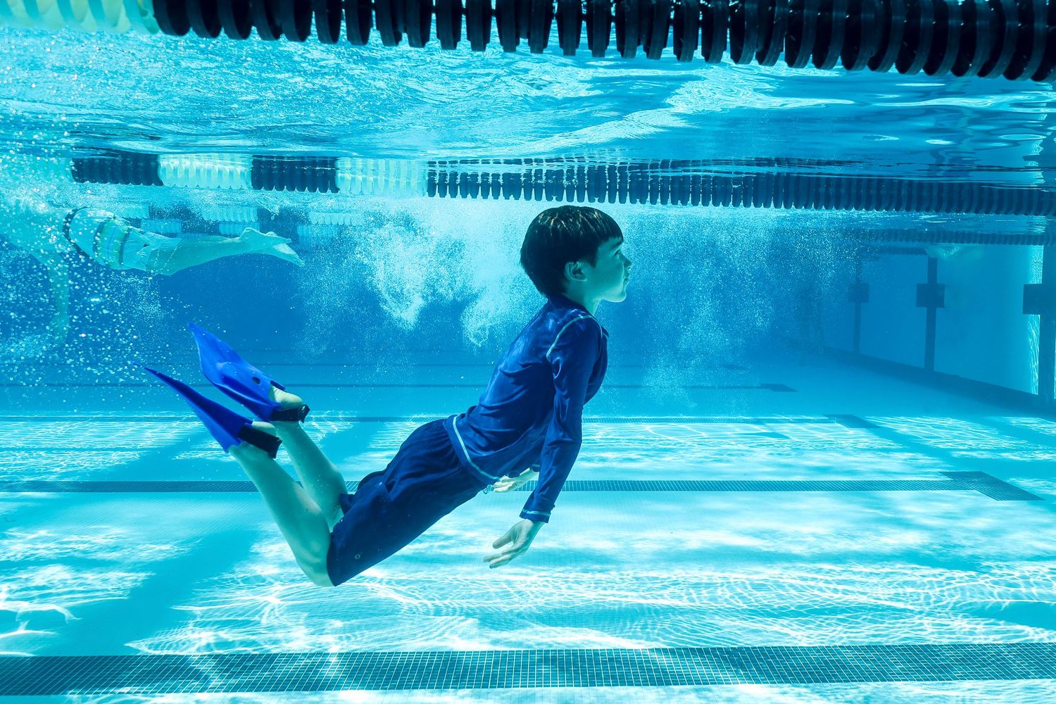 Underwater photography of a child swimming in a pool while wearing blue swim fins, captured by a San Diego photographer.