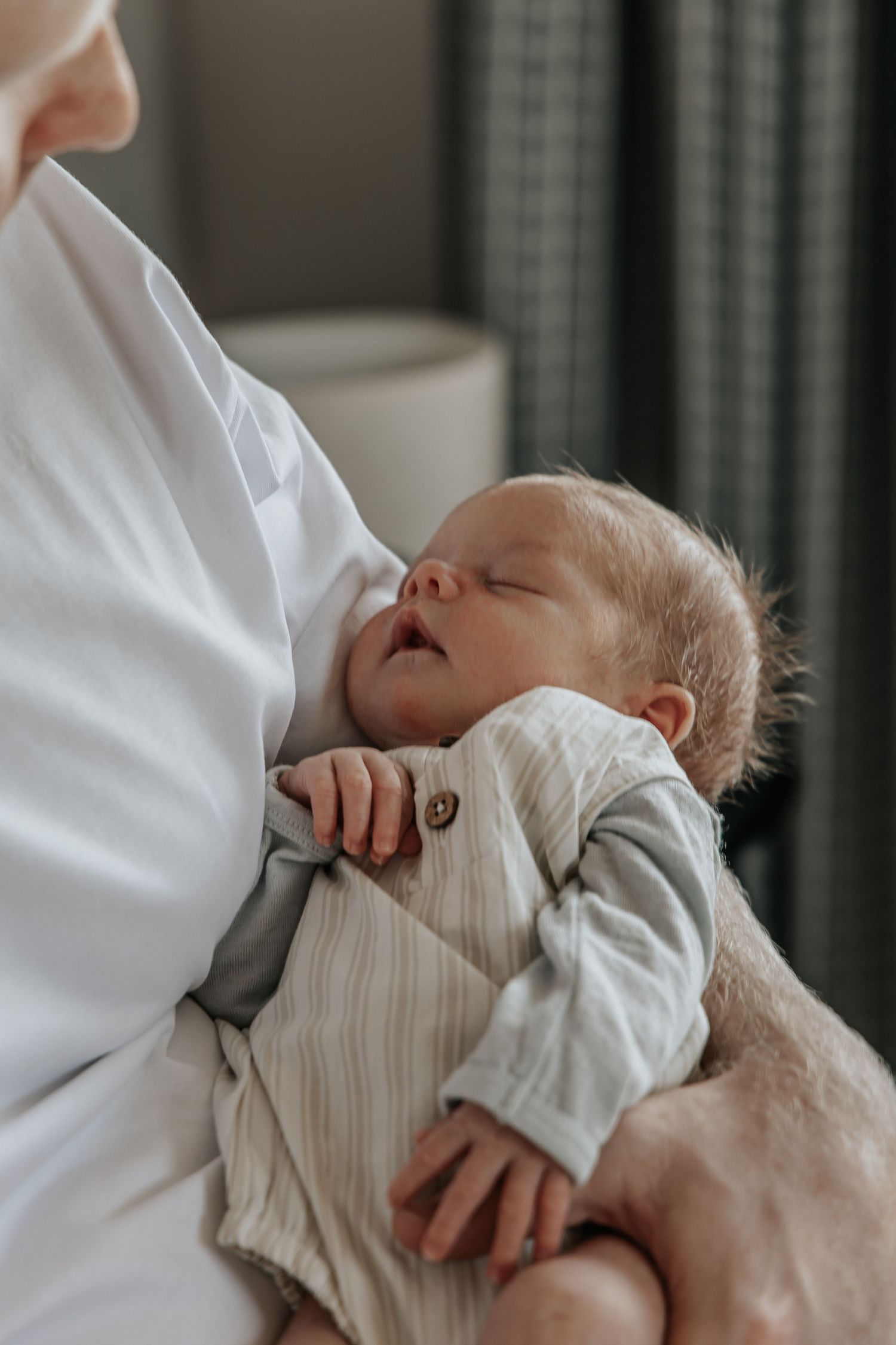 A peaceful newborn baby sleeping in a parent's arms, dressed in a soft striped onesie.