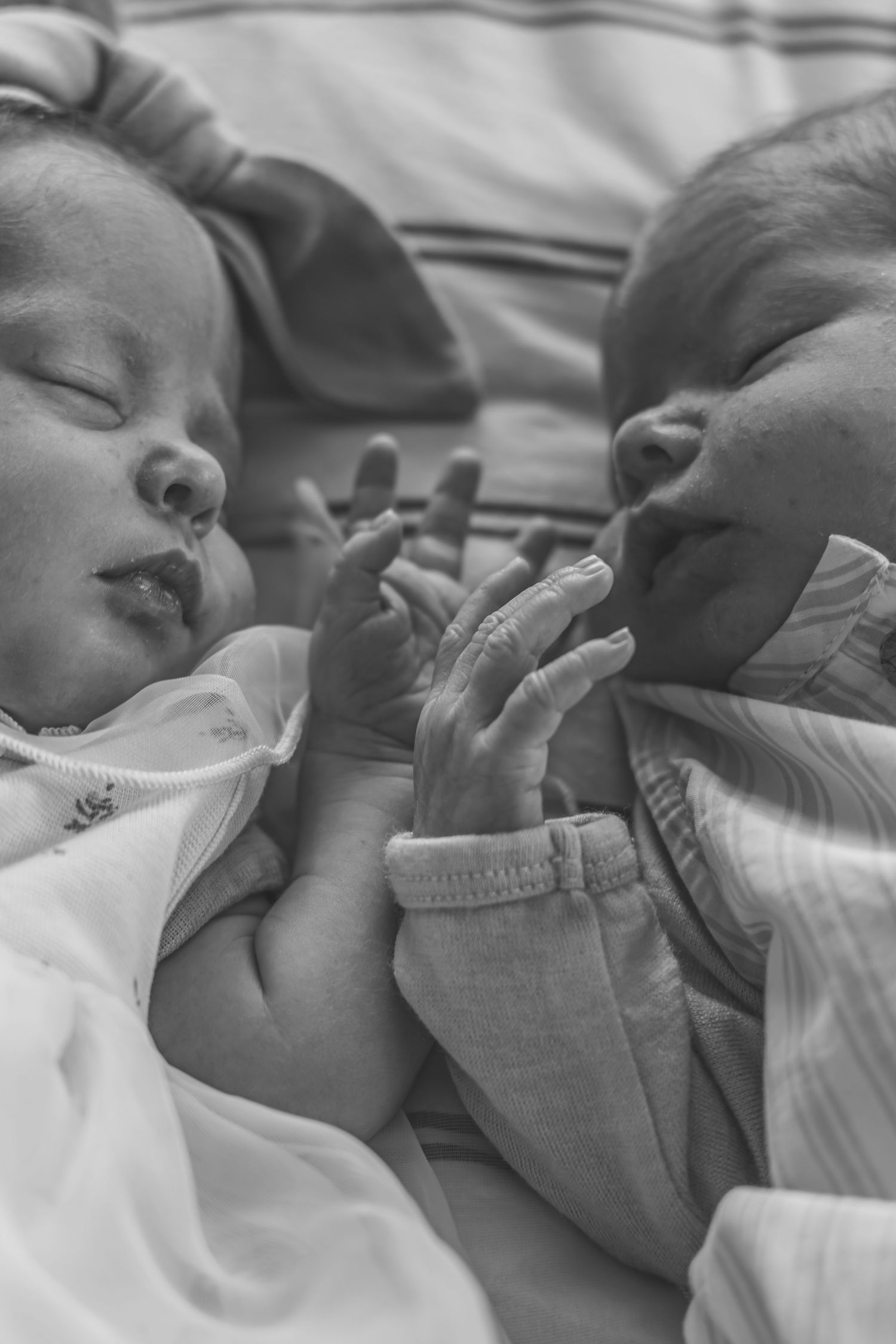 Black and white photo of two newborn twins lying together, gently touching hands in a tender moment.
