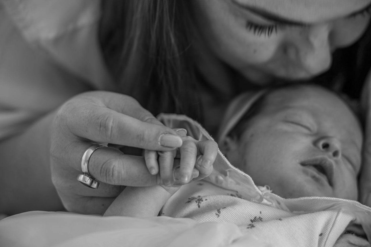 Black and white photo of a mother tenderly holding her newborn baby's hand, capturing a precious bonding moment.