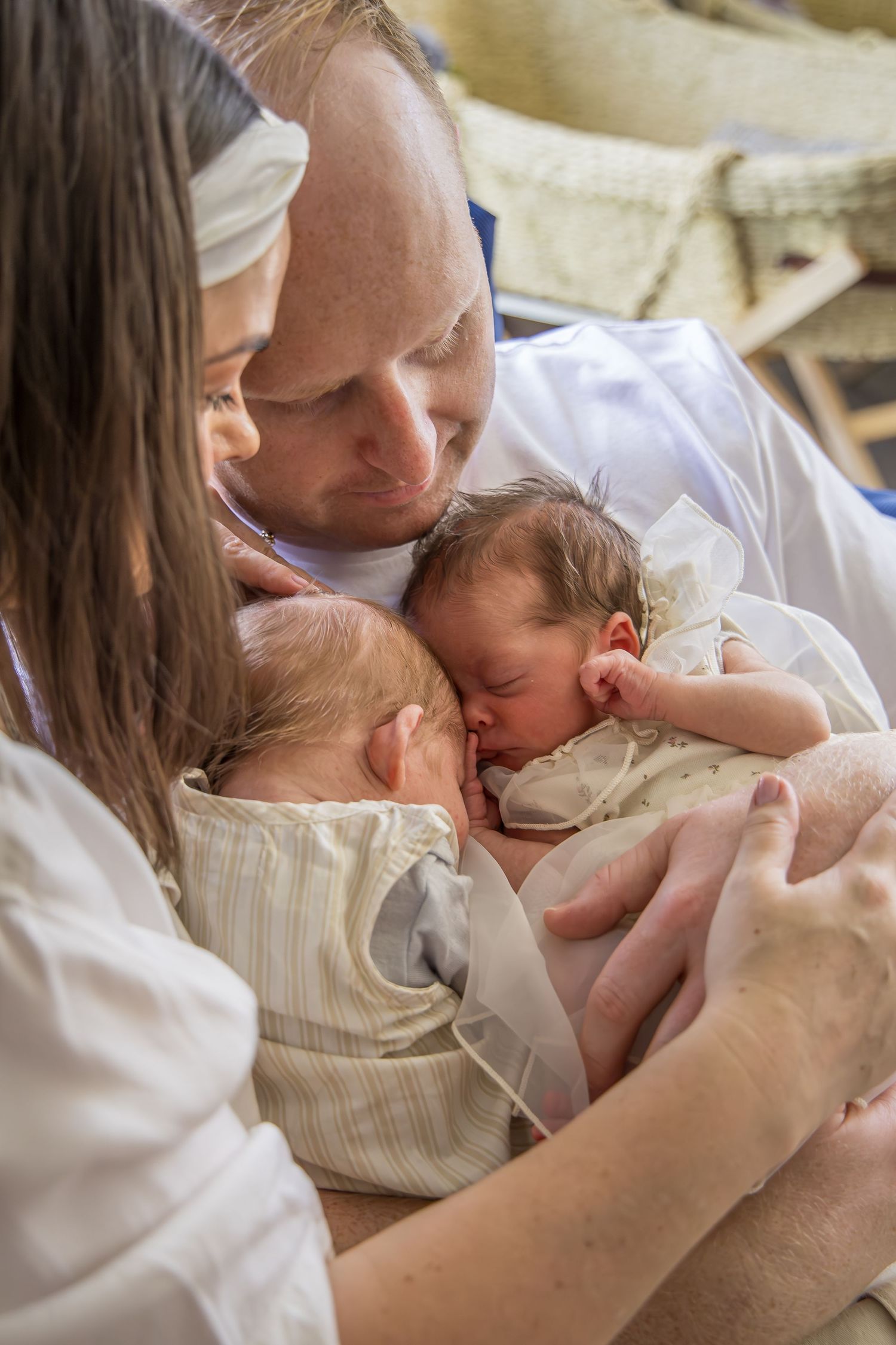 New parents tenderly holding their sleeping newborn twins together in a warm hospital room.