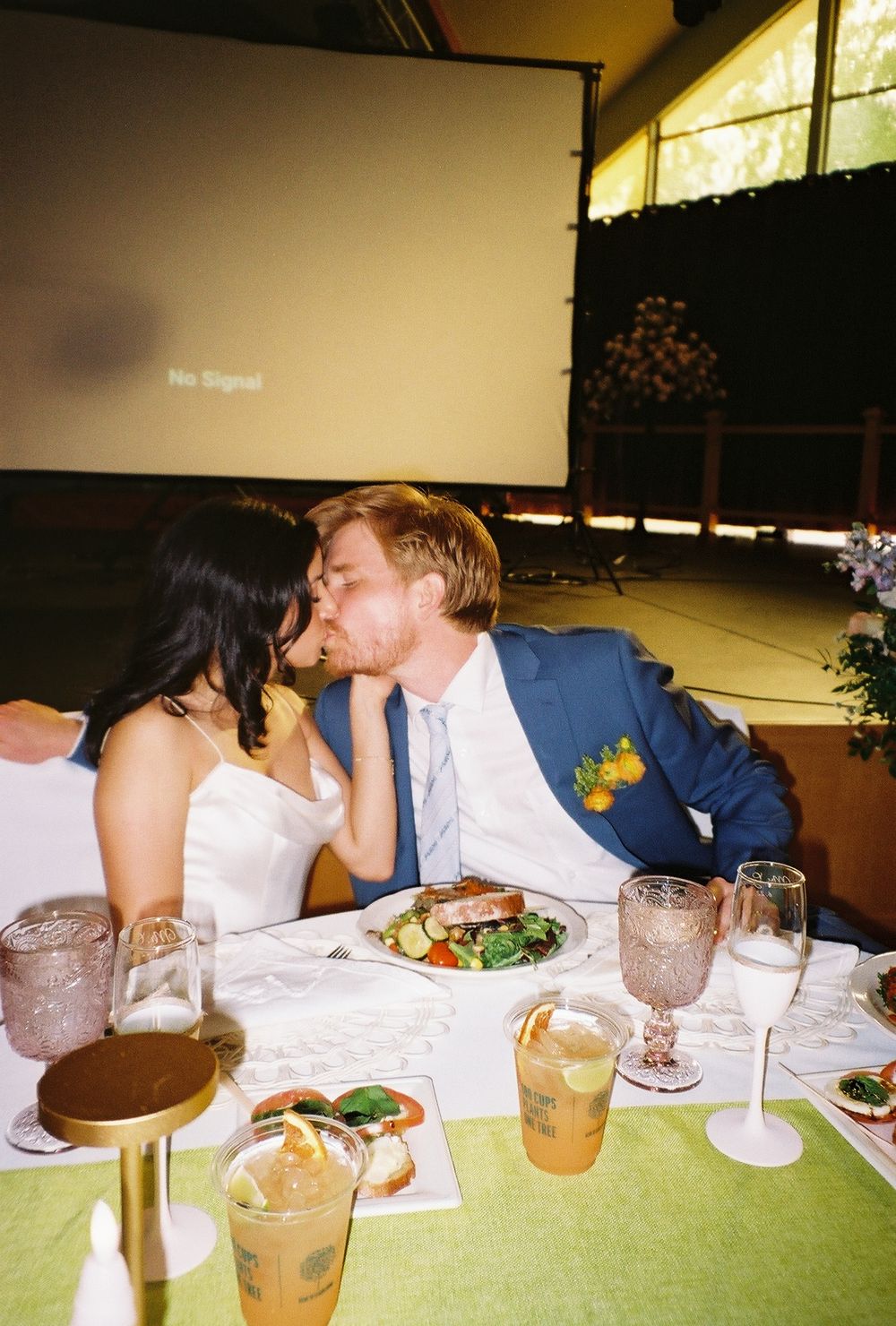 Couple sharing intimate moment at wedding reception table with drinks and food.