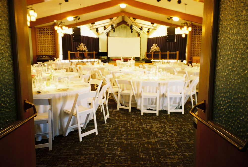Wedding reception hall setup with white tables and chairs arranged for celebration.