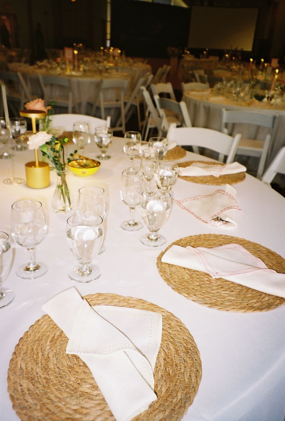 Elegant wedding reception table with white linens, woven placemats and glassware.