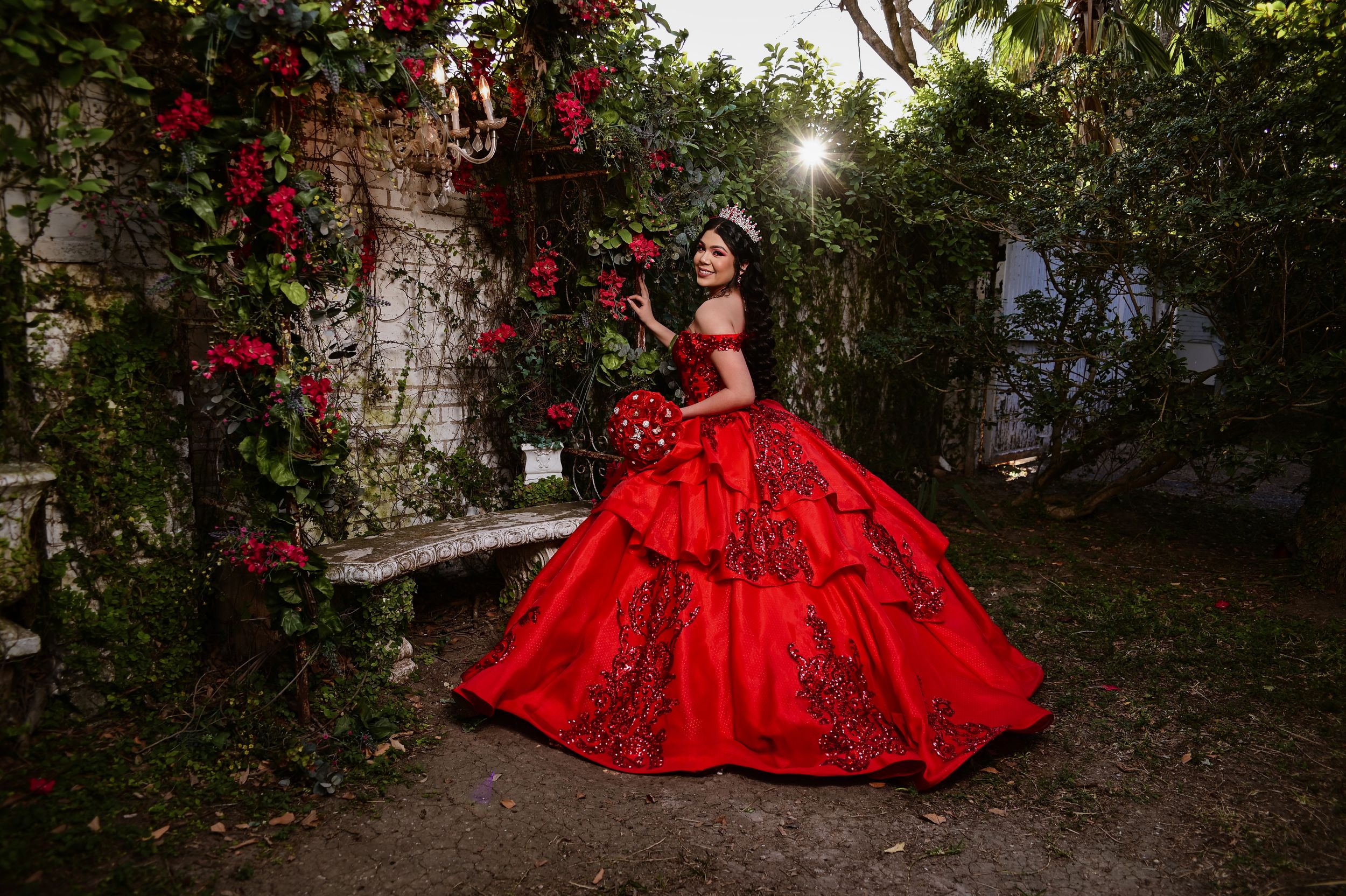 A stunning red ball gown adorned with sparkles photographed in a garden setting with climbing roses.