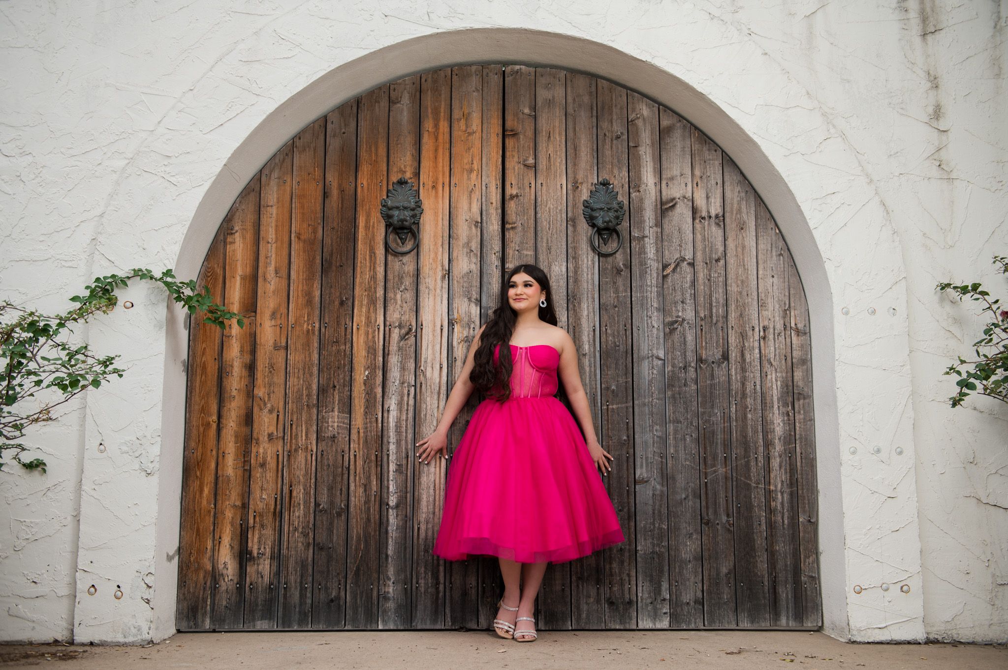 Hot pink tulle dress creates striking contrast against rustic wooden door and white wall.