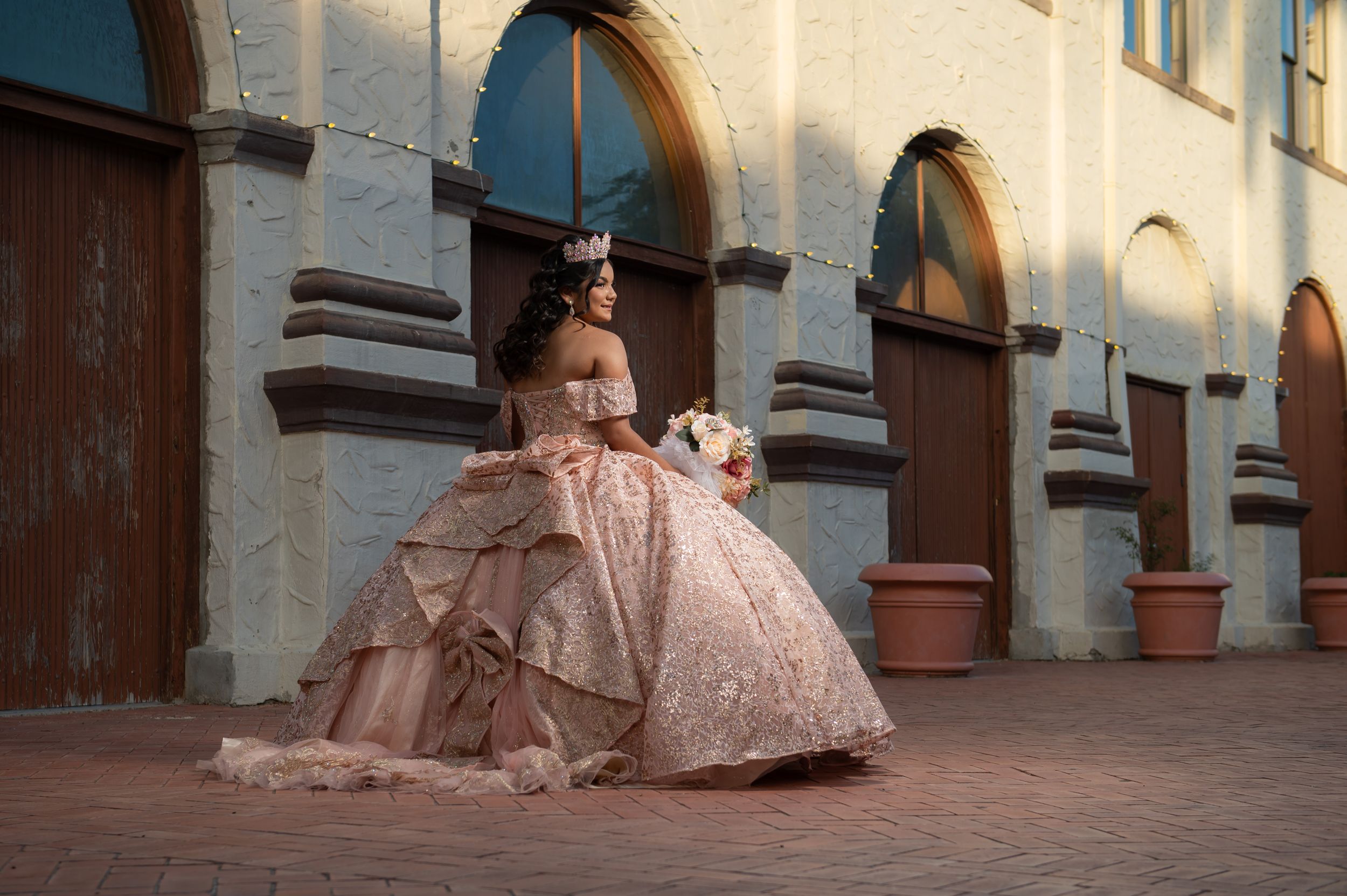 Ornate blush ball gown photographed against classic arched architecture.