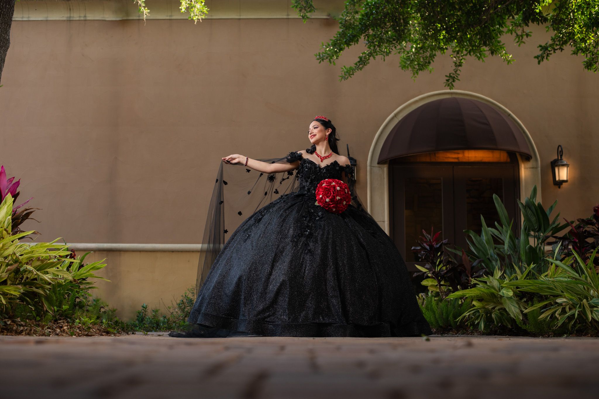 Dramatic black ball gown with red accents photographed against stone archway.