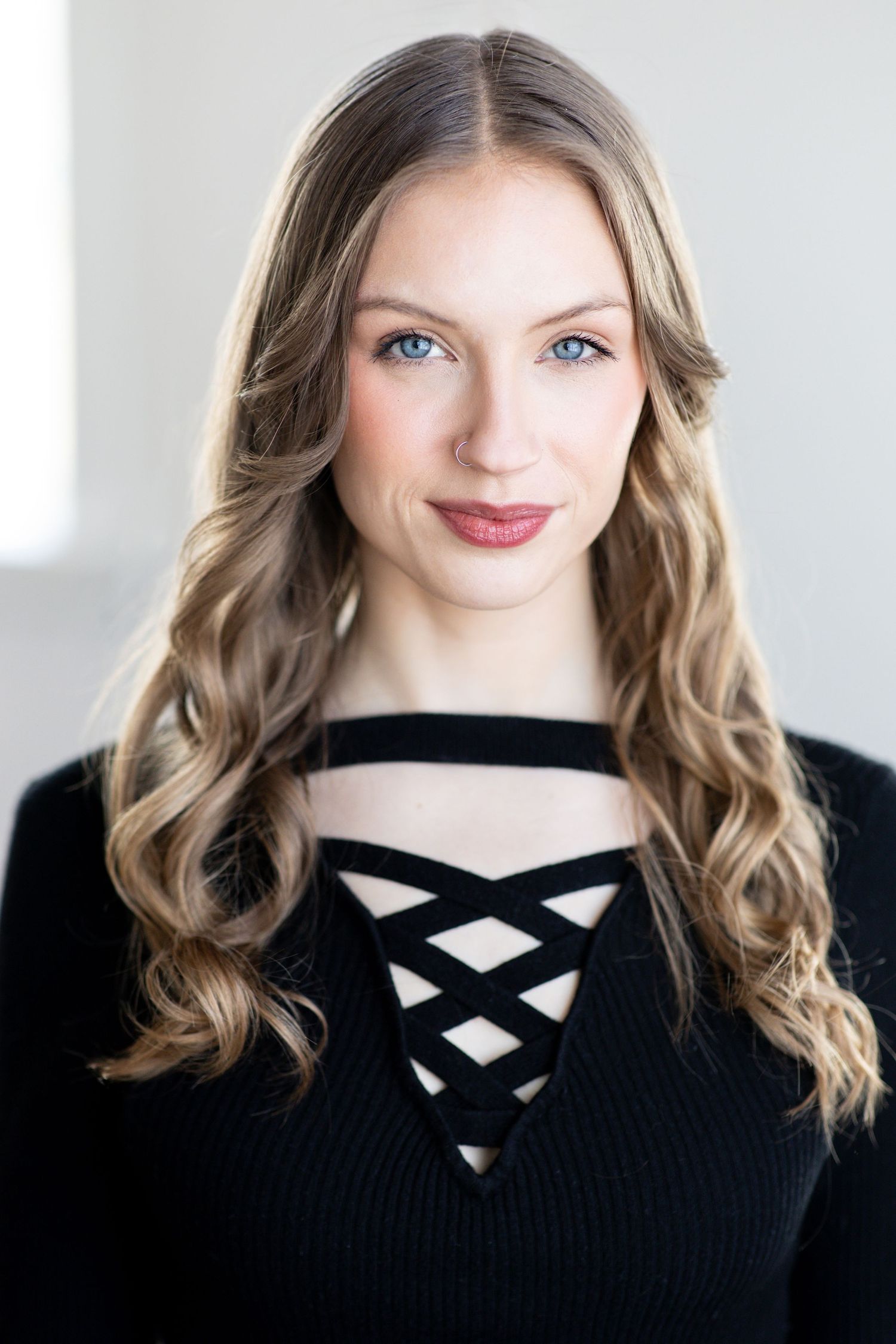 Professional headshot of a performer in a black criss-cross neckline sweater against a light background. Twin Cities headshot photography.