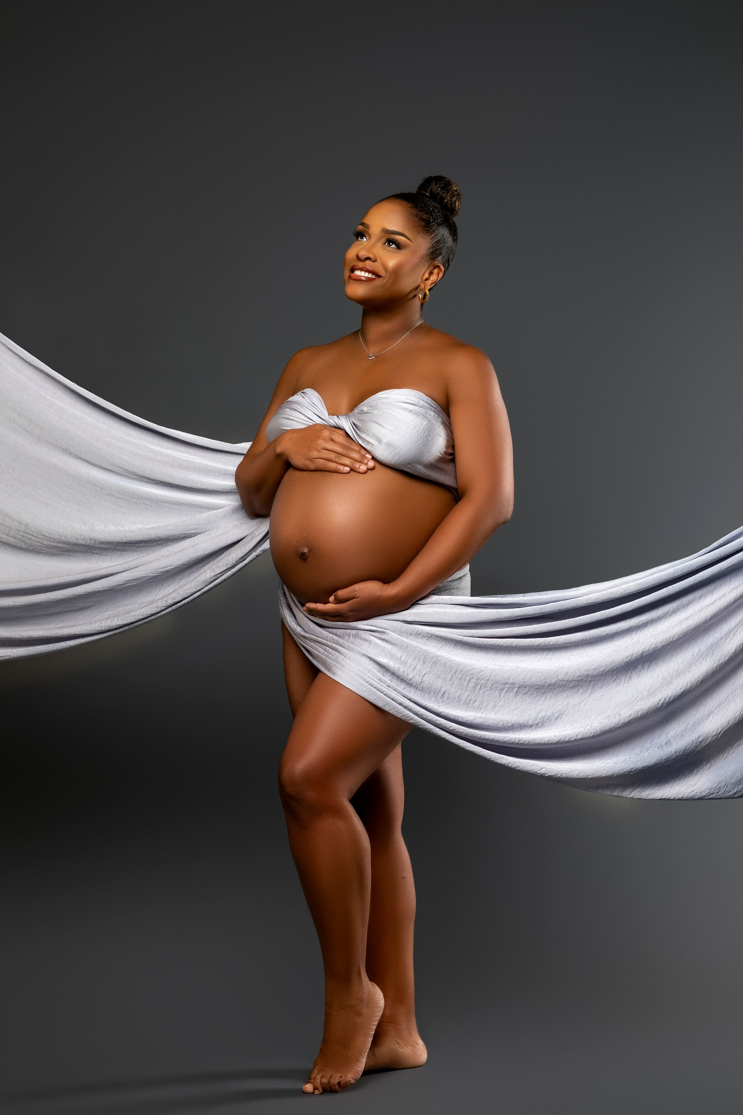 Elegant maternity portrait featuring silver fabric dramatically draped around a pregnant woman wearing silver lingerie.