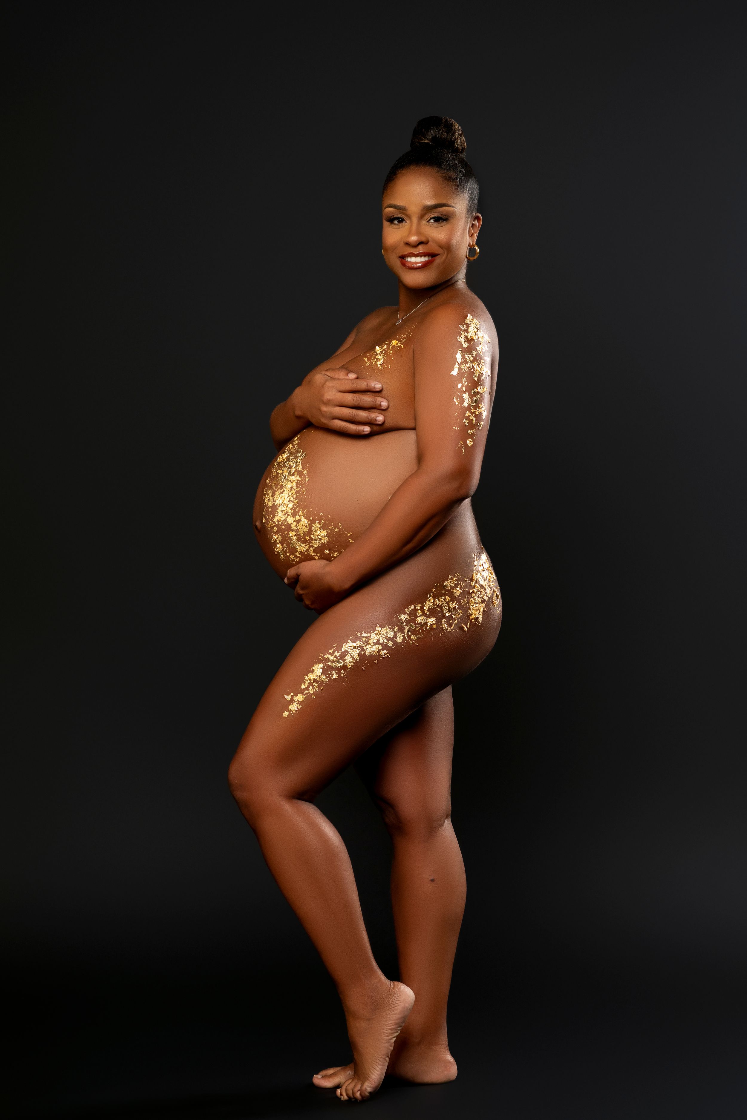 Artistic maternity photo with decorative gold glitter accents against a black background.