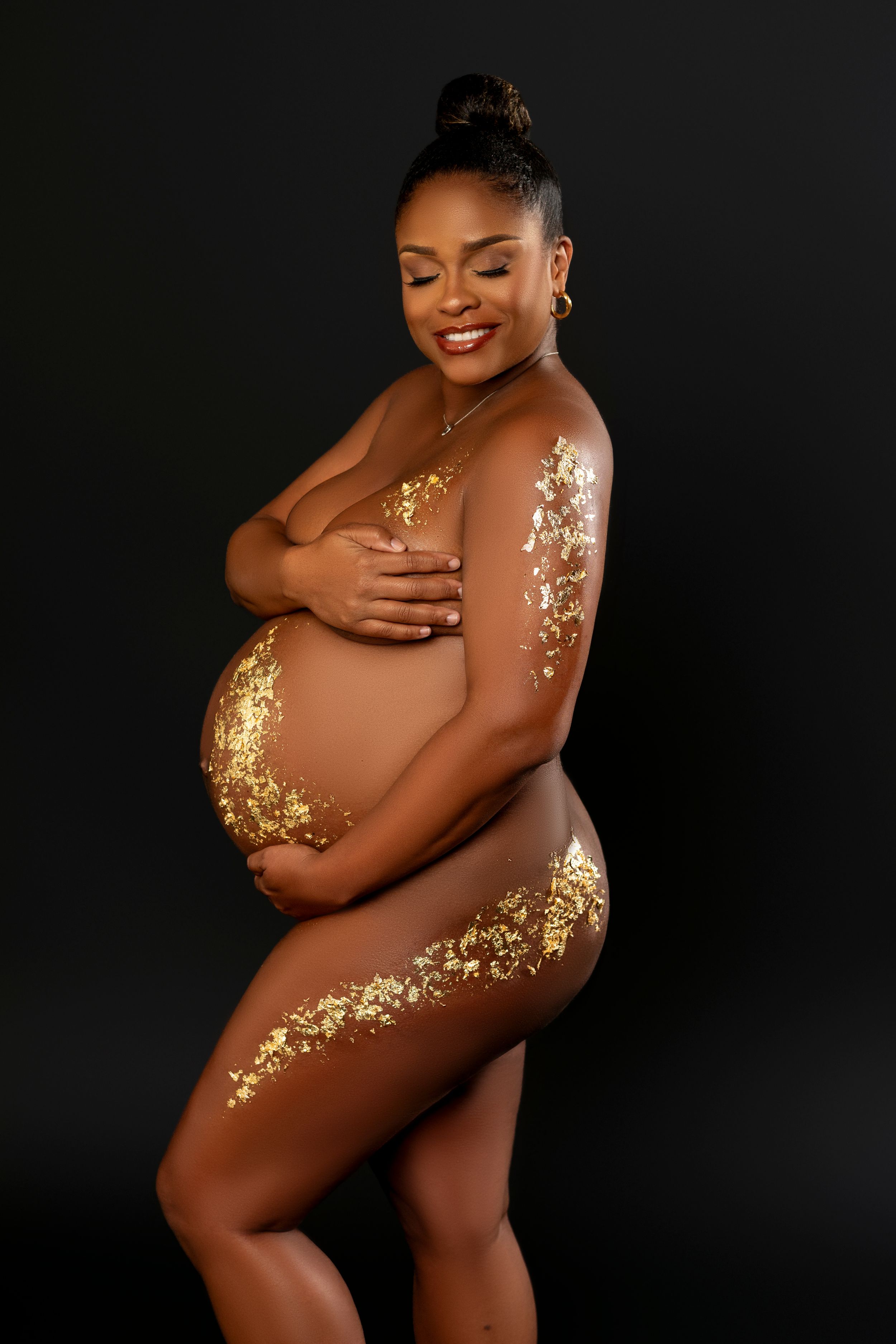 Artistic maternity photo featuring decorative gold leaf accents on dark backdrop in elegant intimate pose.