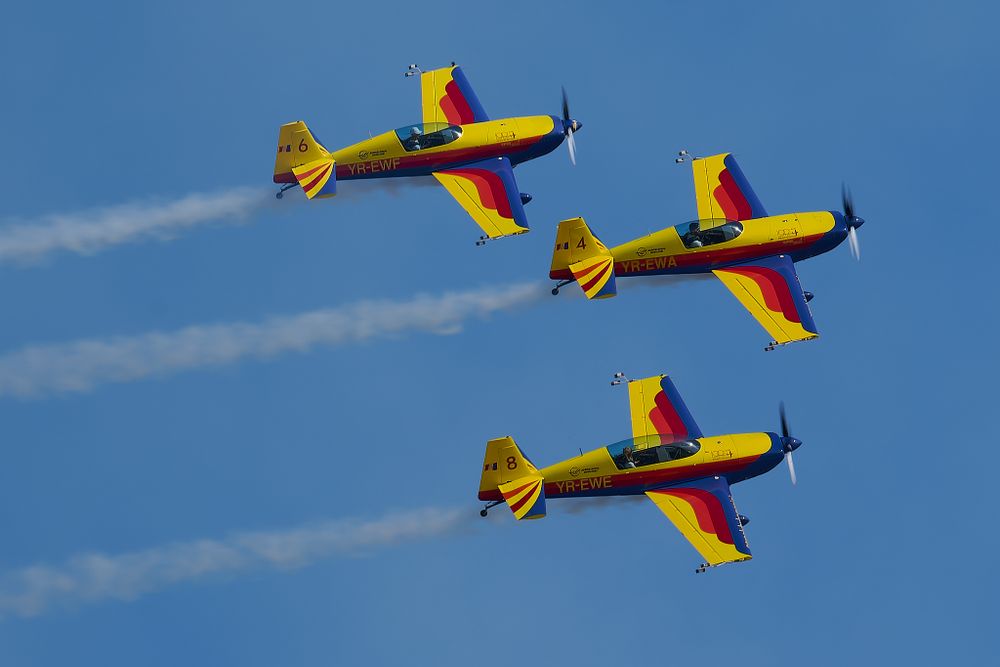 Three yellow and red aircraft fly in formation during an airshow performance.