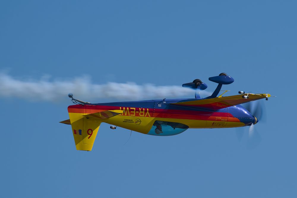 Colorful aerobatic aircraft performs maneuvers against clear blue sky.