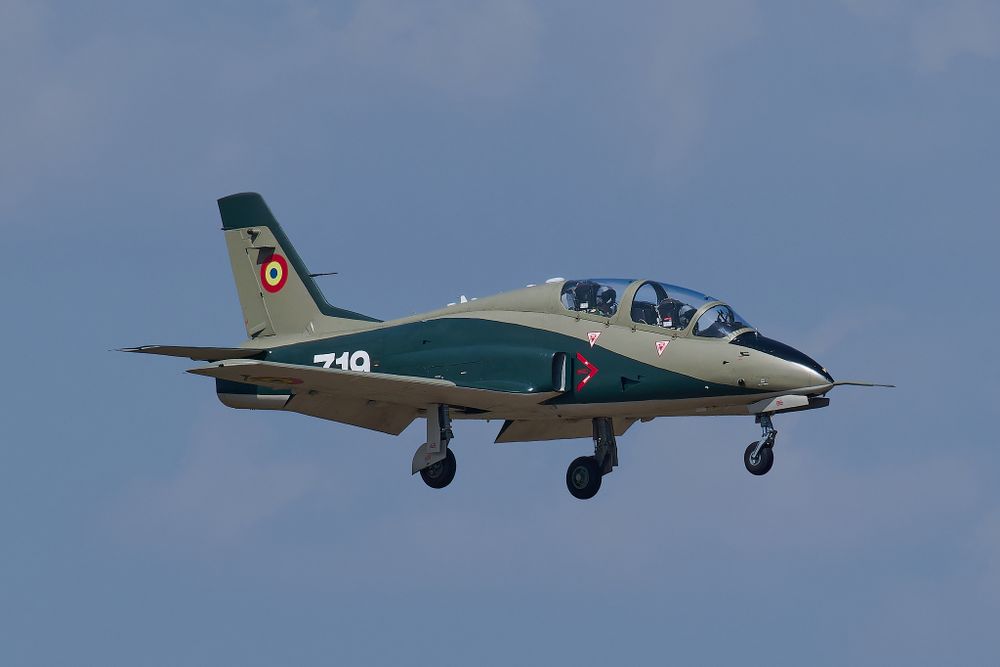 Military training aircraft with green and white paint scheme flying against blue sky.