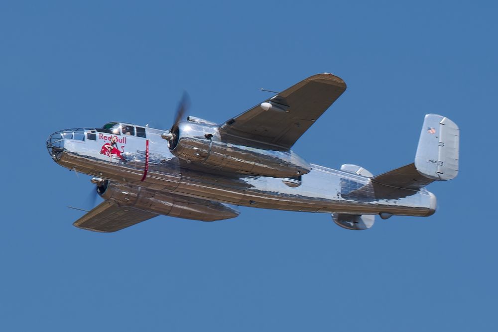 Classic silver B-25 Mitchell bomber aircraft in flight with Red Bull livery.