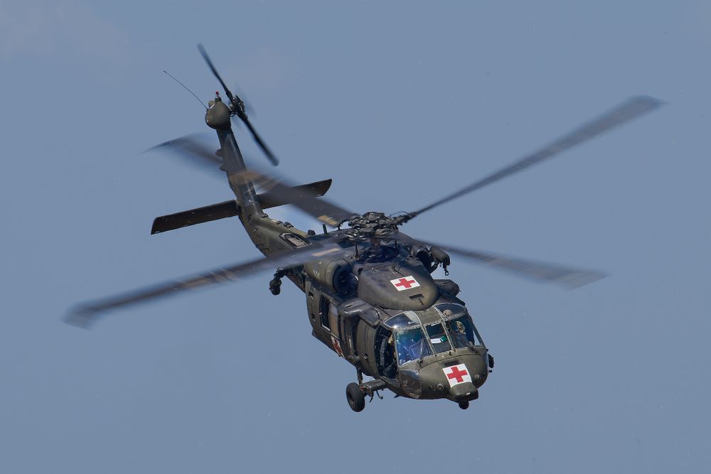 Military Blackhawk helicopter with medical cross emblem flying against clear blue sky.