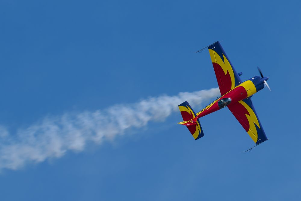 Colorful aerobatic aircraft performing with smoke trail against blue sky.